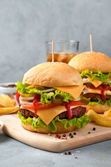 Burgers with meat, cheese and vegetables on the background of cola and French fries.