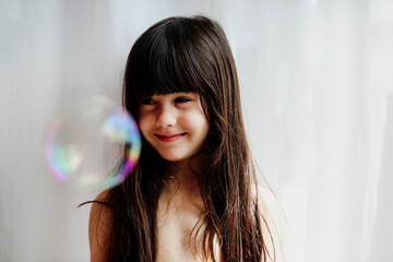 Portrait of a smiling child girl looking  a soap bubble floating
