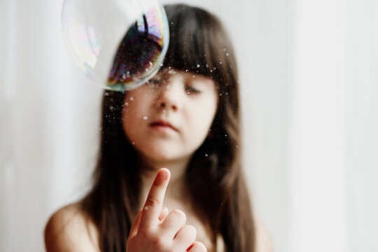 Blurred fantasy portrait of a child girl playing with a soap bubble 