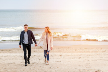 Attractive young couple walking along the shore of a sandy beach, on a spring romantic holiday, outdoors.