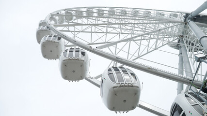 White ferris wheel spinning slowly in amusement park with grey sky in the background. Ride on...