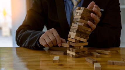 Businessman putting wooden tower blocks on the table, risk control concept. Planning and strategy in the construction and defense business