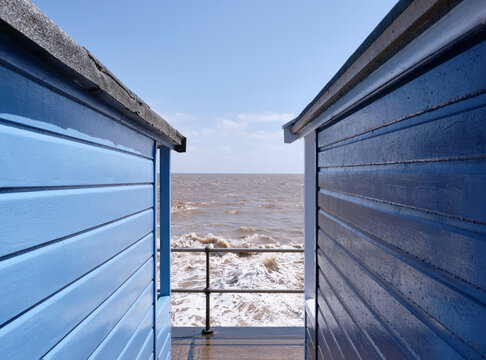 Waves and spray between beach huts. Southwold, Suffolk, UK.