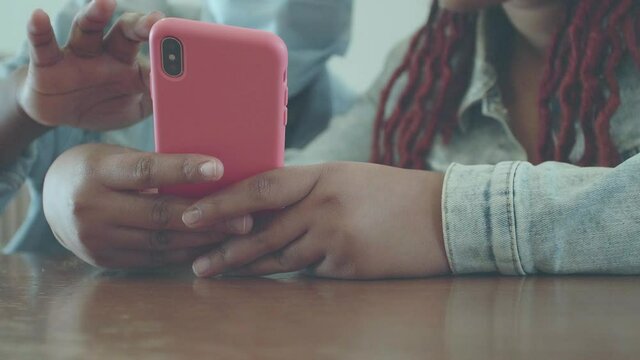 A smartphone in a pink case in the hands of an afro woman and another woman touches the screen with her hand