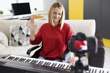 Young woman playing piano and waving to camera at home