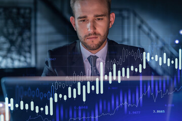 Handsome businessman in suit at workplace working with laptop to optimize trading strategy at...