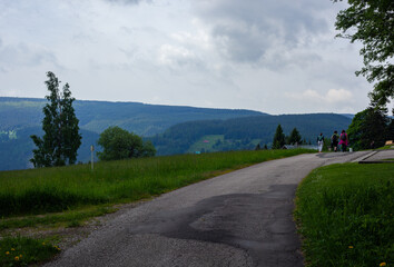 Une vue sur les montagnes du nord de la République tchèque avec un ciel gris rempli de nuages et trois personnes de dos marchant.