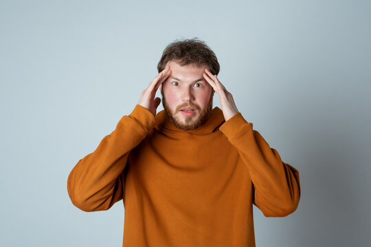 Troubled bearded young man cover head with hands and looking worried, panicking, staring alarmed at something shocking