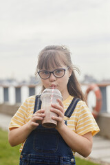 Vertical portrait of carefree girl with down syndrome drinking milkshake outdoors and looking at...