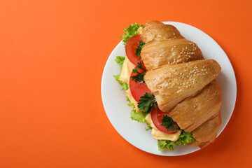 Plate with croissant sandwich on orange background