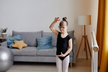 Waist up portrait of cute girl with down syndrome doing ballet exercises at home and looking at camera, copy space