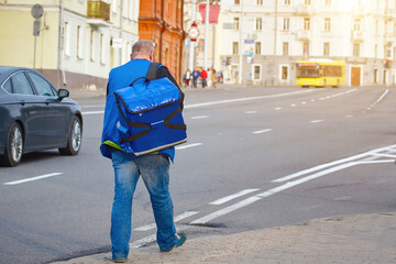 Man deliver food, walking with blue thermal backpack. Delivery service worker with thermal backpack at city street. Delivering fast food from favourite restaurant, supermarket or cafe