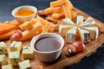 Assortment of cheese. Composition of different varieties of cheese with honey, nuts, olives on rustic dark wooden desk