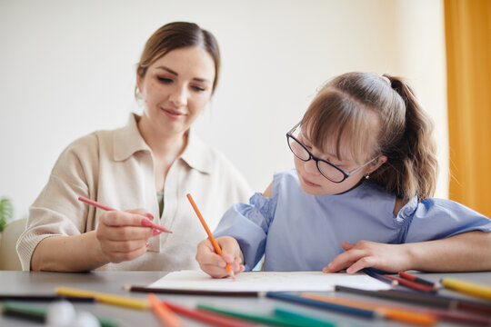 Portrait of cute teenage girl with down syndrome doing homework with caring mother helping her