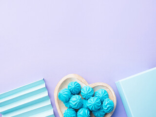 Blue turquoise meringue on heart shaped dish with gift box and decor on pastel purple background