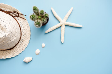 Ein Seestern, ein Sonnenhut, ein Kaktus und kleine weiße Muscheln auf einem blauen Hintergrund....