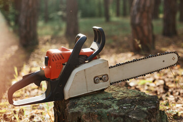 Outdoor closeup shot of chainsaw on stump in wood, professional equipment for cutting wood, deforestation, logging, special tool for working with forestry.