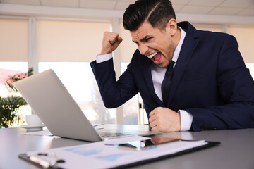 Emotional businessman with laptop at table in office
