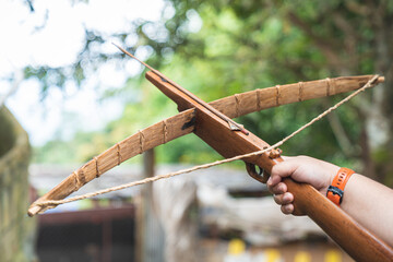 A crossbow made of ordinary wood used by hill tribes to hunt. He was held in his right hand aiming towards the sky with a blurred background of sky and trees.