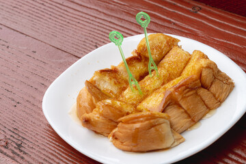 Toasted bread buttered and topped with sweetened condensed milk was placed in a white plate on a wooden table.