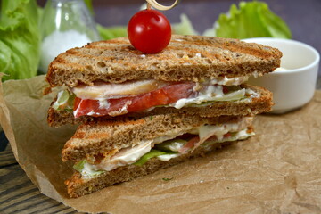 Club Sandwich with Cheese, PIckled Cucumber, Tomato and Smoked Meat. Garnished with sauce on wooden table