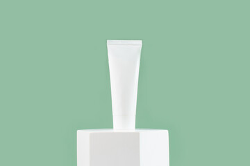 White cosmetic tube for skin care face, body on white podium on green background..