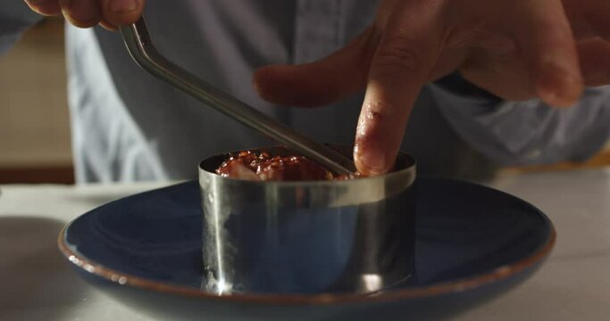 Cook plating octopus on plate topping with olive oil creating an octopus and potatoes dish in a well appointed kitchen with an array of a equipment and appliances. Close up shot on 4k RED camera.