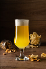 light beer unfiltered with a large strong white foam on a wooden background, copyspace. With beer snacks
