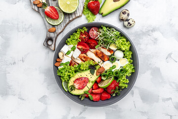 Lunch bowl with chicken, avocado, feta cheese, quail eggs, strawberries, nuts and lettuce. Detox and healthy superfoods bowl concept. top view