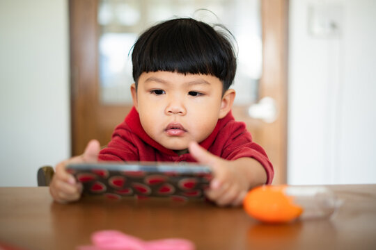 Asian kid watching smartphone on Dining table