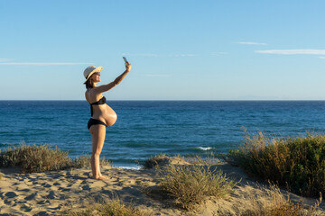 Pregnant young woman making a selfie with her phone on the beach