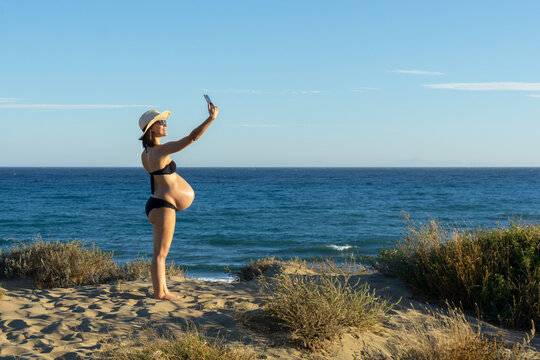 Pregnant young woman making a selfie with her phone on the beach