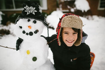 boy hugging snowman in front of house