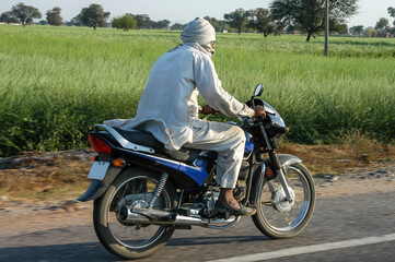 Fototapeta na wymiar Campesino circulando en motocicleta por una carretera de Rajastán en India