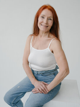 Smiling Senior Woman in jeans sitting in studio