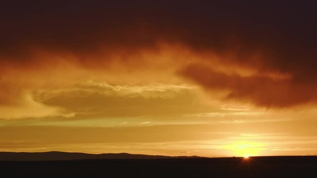 Colorful Wyoming sunset as cars move across the sun on the horizon in timelapse.