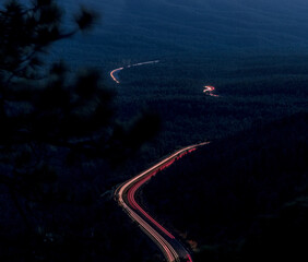 Looking down from a forest mountain ledge at the roadway trailing through a pine forest at night...