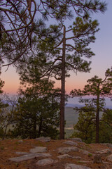 Obraz na płótnie Canvas In Payson, Arizona this is known as the Mogollon Rim. The sun sets looking out over the rim, through the trees, the colorful sky paints the ledge and flowing hills, boulders and trees colorful shades 