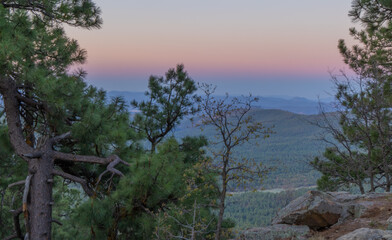 In Payson, Arizona this is known as the Mogollon Rim. The sun sets looking out over the rim, through the trees, the colorful sky paints the ledge and flowing hills, boulders and trees colorful shades 