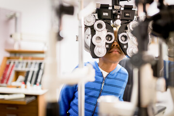 Boy peers through phoropter at optometrist