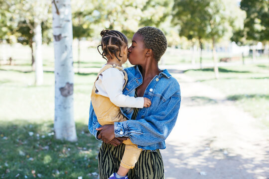 African American mother kissing daughter in summer park
