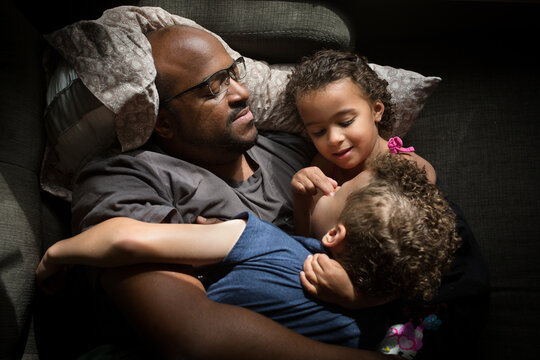 Girl snuggles father and brother on couch