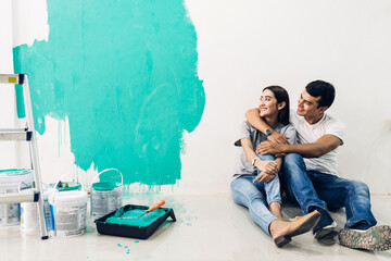 Naklejka premium Happy couple using a paint roller and painting walls in their new home