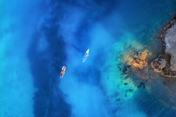 Aerial view of people on floating sup boards on blue sea, rocks, stones at sunset in summer in...
