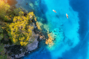Aerial view of people on floating sup boards on blue sea, rocks, trees at sunset in summer. Blue lagoon, Oludeniz, Turkey. Tropical landscape. Kayaks on clear water. Active travel. Top view of canoe
