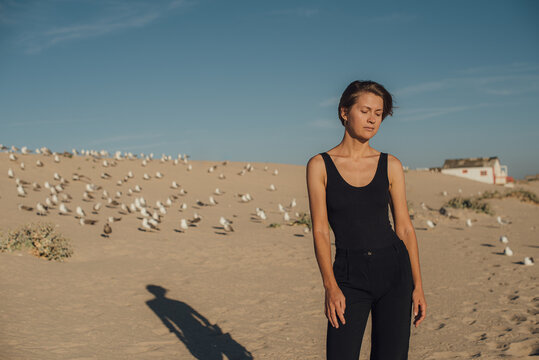 Woman standing in the sand dune with a group of birds on the background