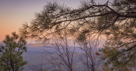 Obraz premium In Payson, Arizona this is known as the Mogollon Rim. The sun sets looking out over the rim, through the trees, the colorful sky paints the ledge and flowing hills, boulders and trees colorful shades 