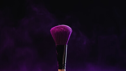 cosmetic brush with purple holi powder near dust on black background