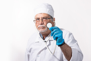 An experienced elderly doctor in a white medical coat and cap with a phonendoscope in his hands.