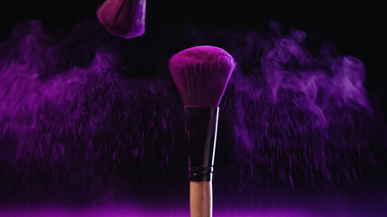 soft cosmetic brushes with holi paint near pink splash of dust on black background